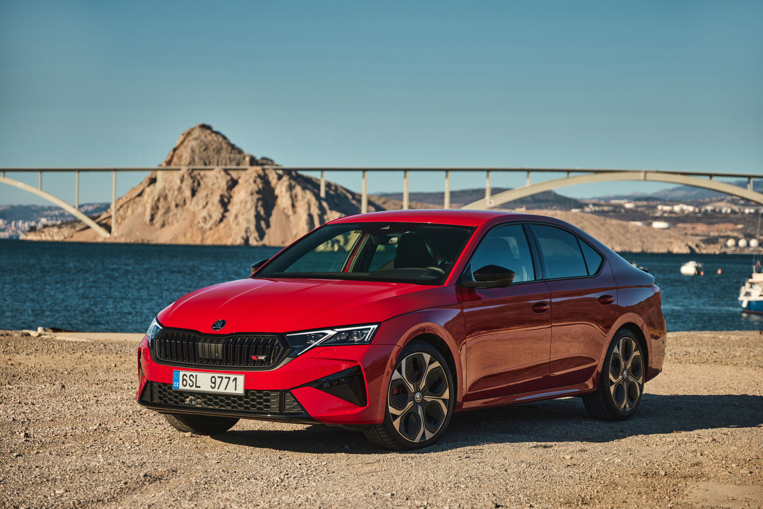 2025 Skoda Octavia RS in red parked by a seaside backdrop with a bridge and mountains