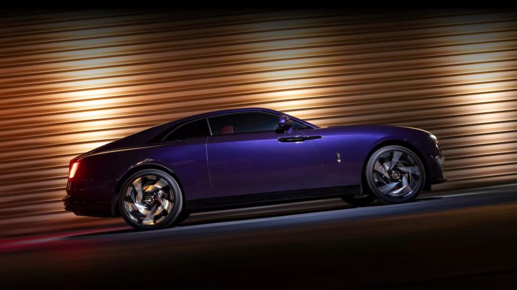 Rolls-Royce Spectre driving at night with golden lights reflecting on body